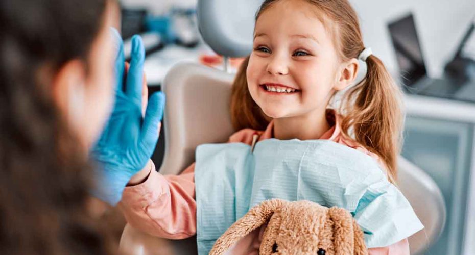 At the doctor's appointment. A candid emotional photo of a child sitting in a dental chair, holding a toy rabbit and cheerfully giving a high-five to the nurse.