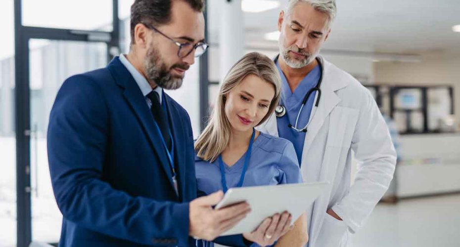 Pharmaceutical sales representative talking with doctors in medical building, presenting new medication on tablet. Hospital director, manager in modern clinic with doctor and nurse.