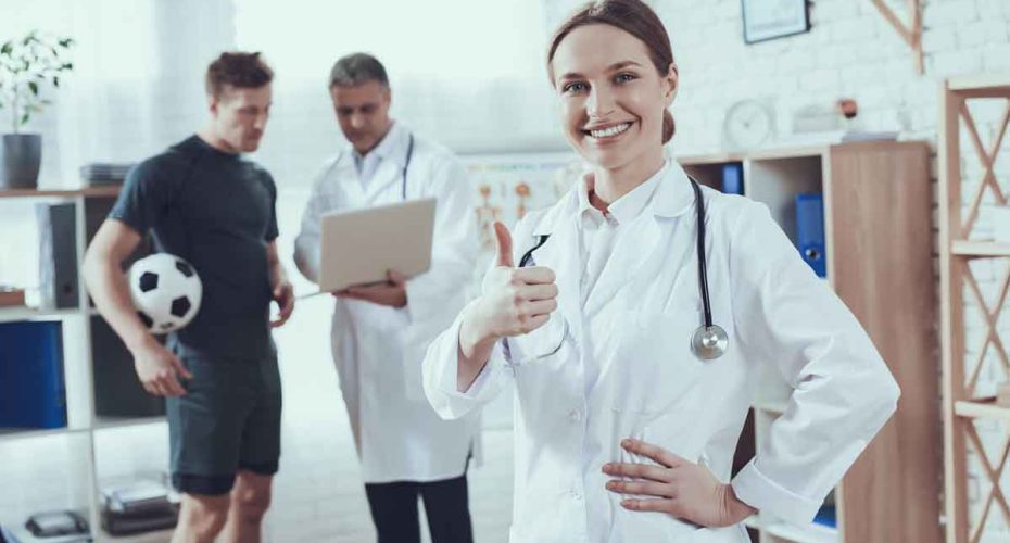 Woman doctor with stethoscope on shoulders shows super gesture. The footballer came to see two doctors with an injury.